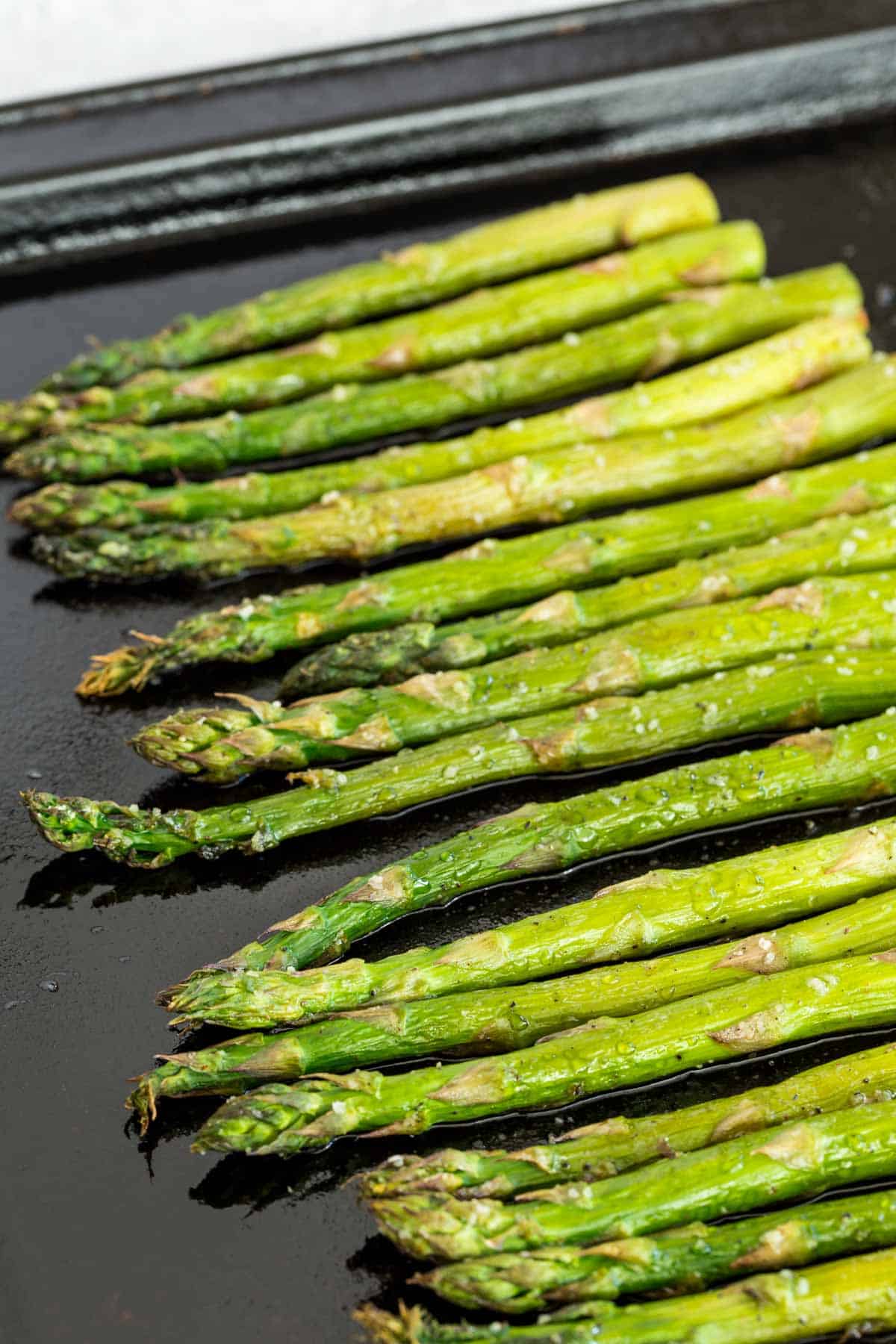 Roasted asparagus spears lined up on a sheet pan.