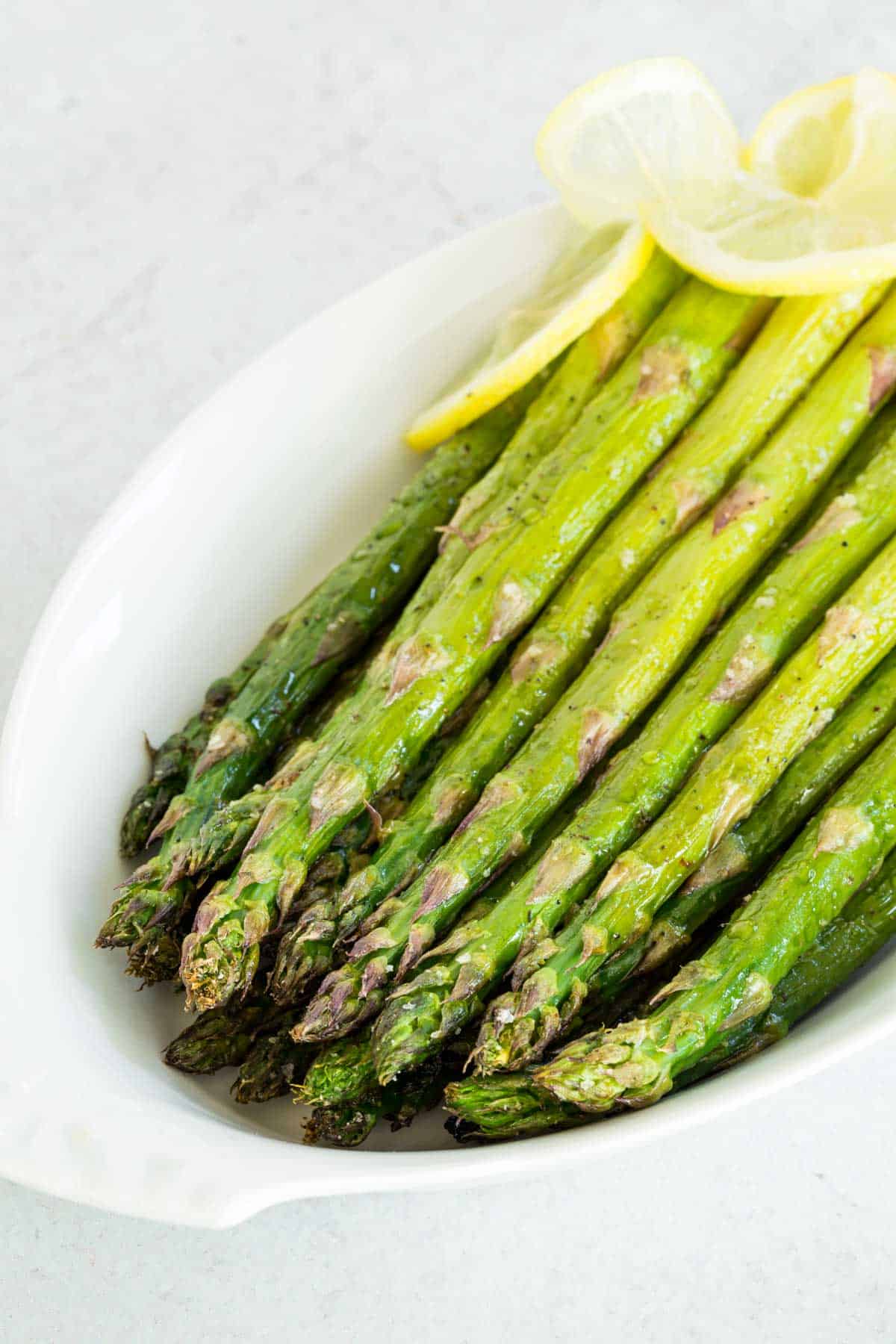 Oven-roasted asparagus garnished with lemon sliced and served in a white oval dish.