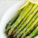 Oven-roasted asparagus in a white serving dish with some pieces of lemon as a garnish.