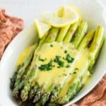 A serving dish of asparagus with hollandaise sauce on top and a garnish of parsley.
