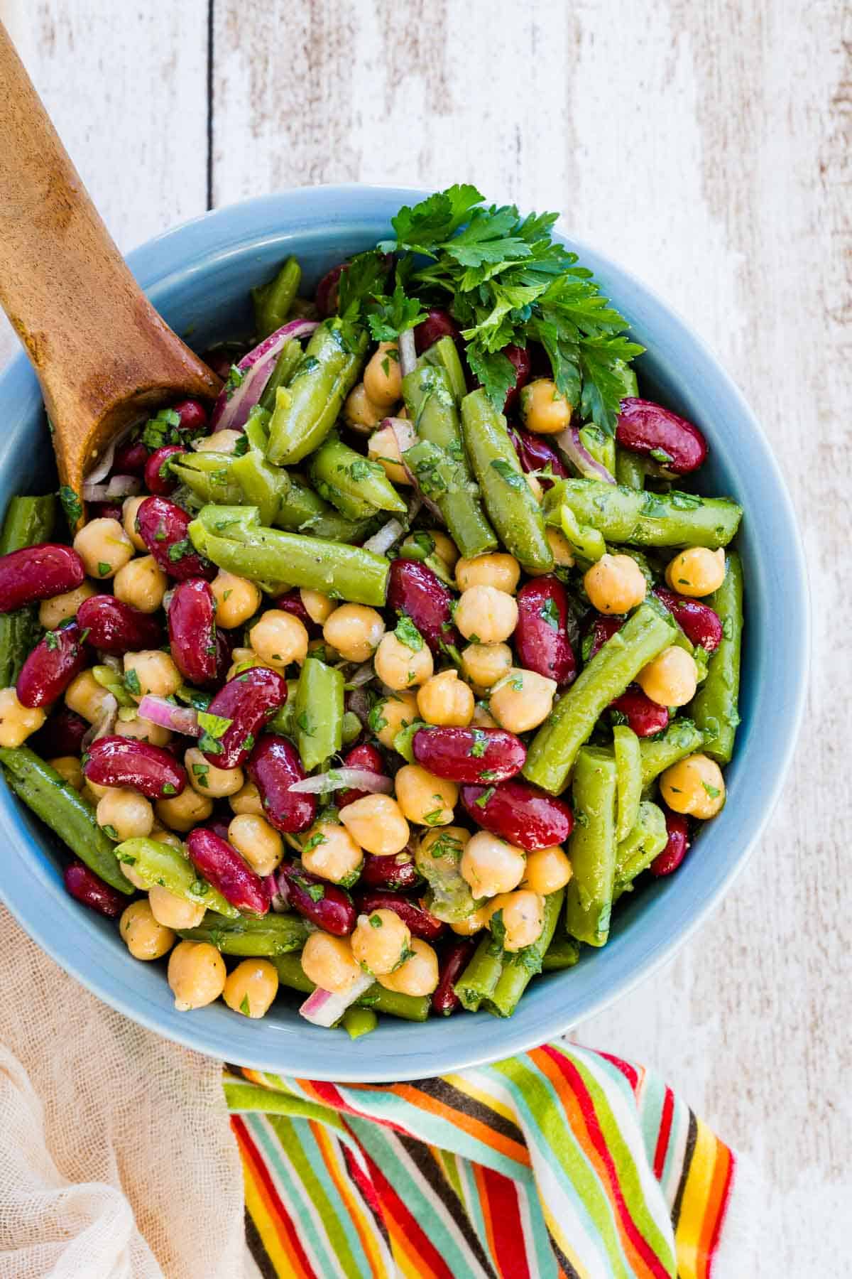 Top view of three bean salad in a blue bowl with a wooden spoon.