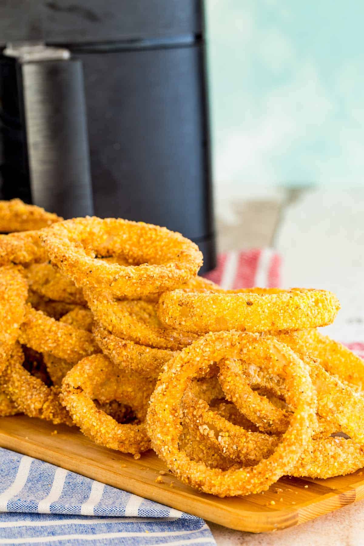 Crispy air fryer onion rings on a rectangular wooden serving tray in front of the air fryer.