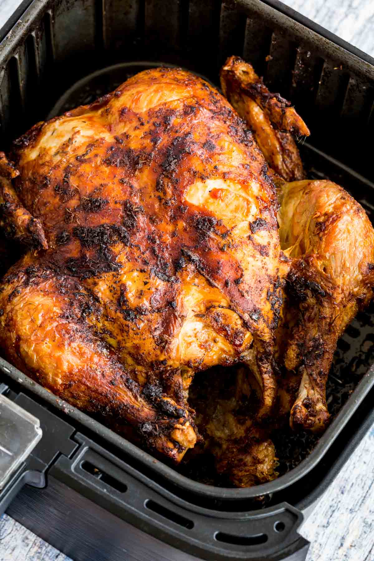 A cooked whole rotisserie chicken inside an air fryer basket.