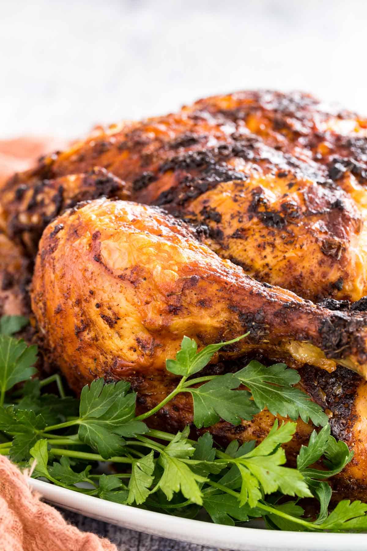 Close up of air fryer rotisserie chicken in a platter garnished with greens.