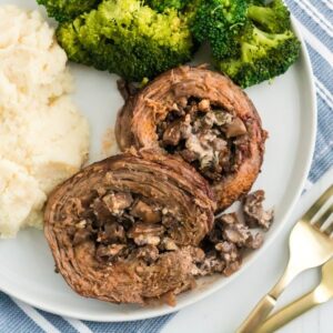 Two mushroom-stuffed flank steak pinwheels on a plate with broccoli and mashed ptoatoes.