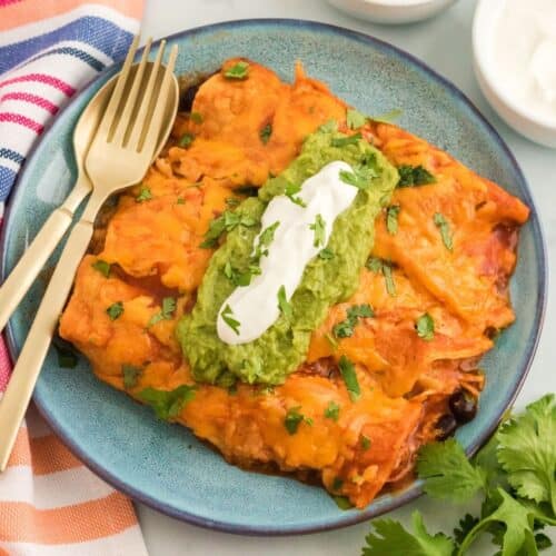 Three cheesy chicken enchiladas on a plate topped with guacamole and sour cream.