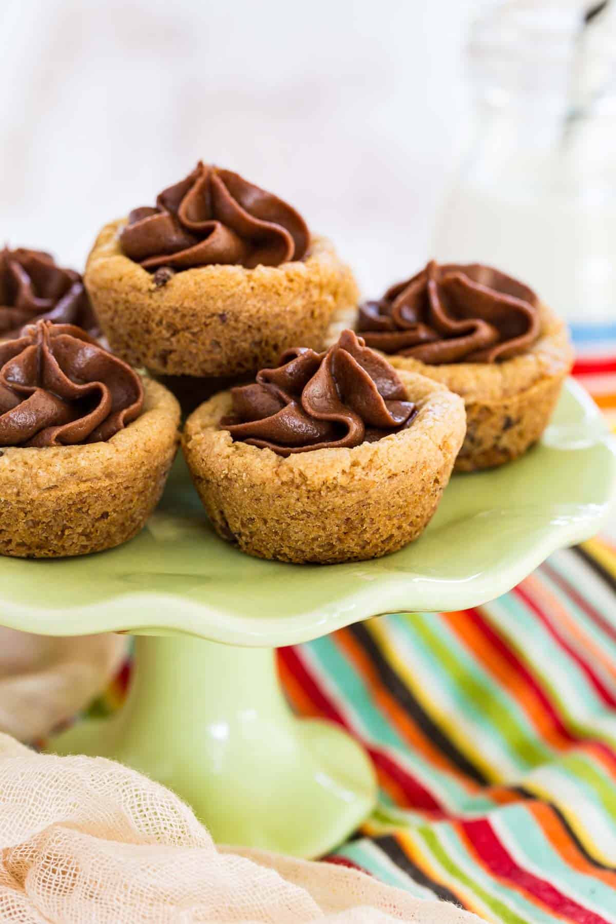 Gluten free chocolate chip cookie cups filled with swirls of chocolate frosting on a green cake stand.