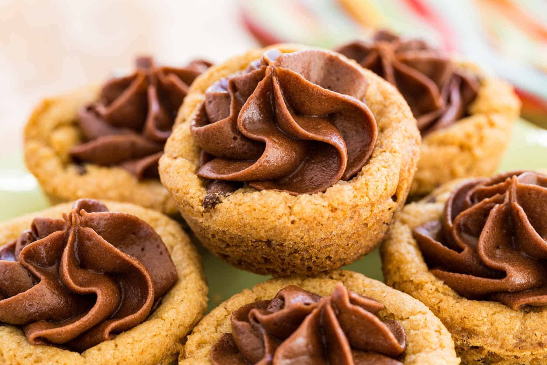 Gluten free chocolate chip cookie cups filled with swirls of chocolate frosting on a green cake stand.