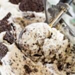 An ice cream scoop scooping cookies and cream ice cream from a tub.