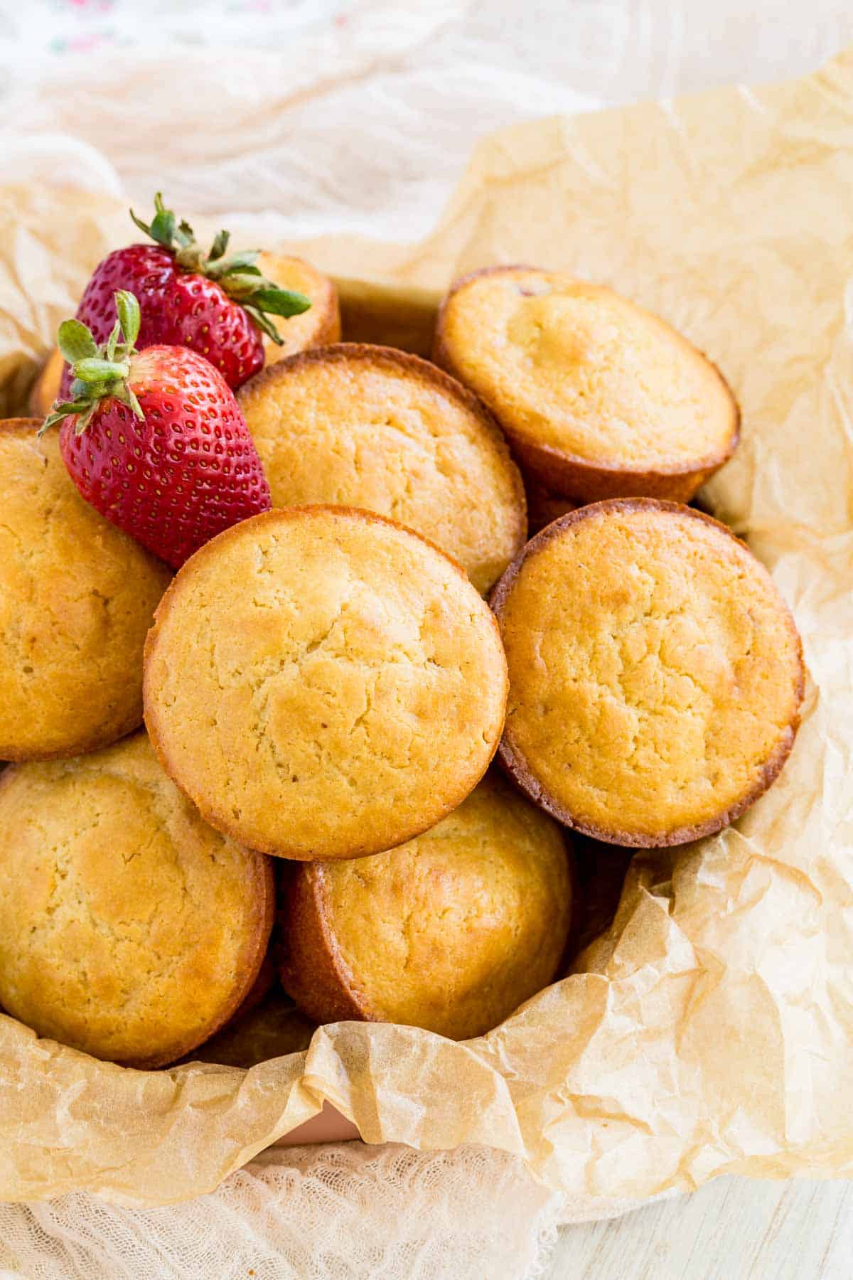 Gluten free strawberry muffins in a bowl with two fresh strawberries.