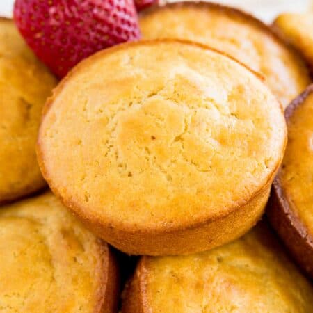 Gluten free strawberry muffins in a bowl with two fresh strawberries.