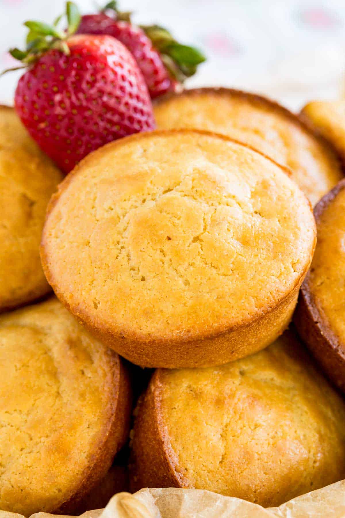 Gluten free strawberry muffins in a bowl with two fresh strawberries.