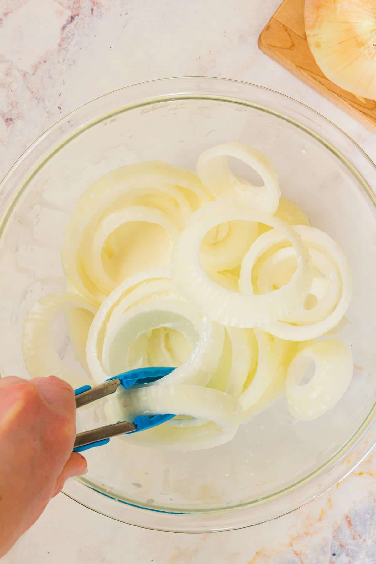 Onion slices are dipped into a bowl of milk coating.