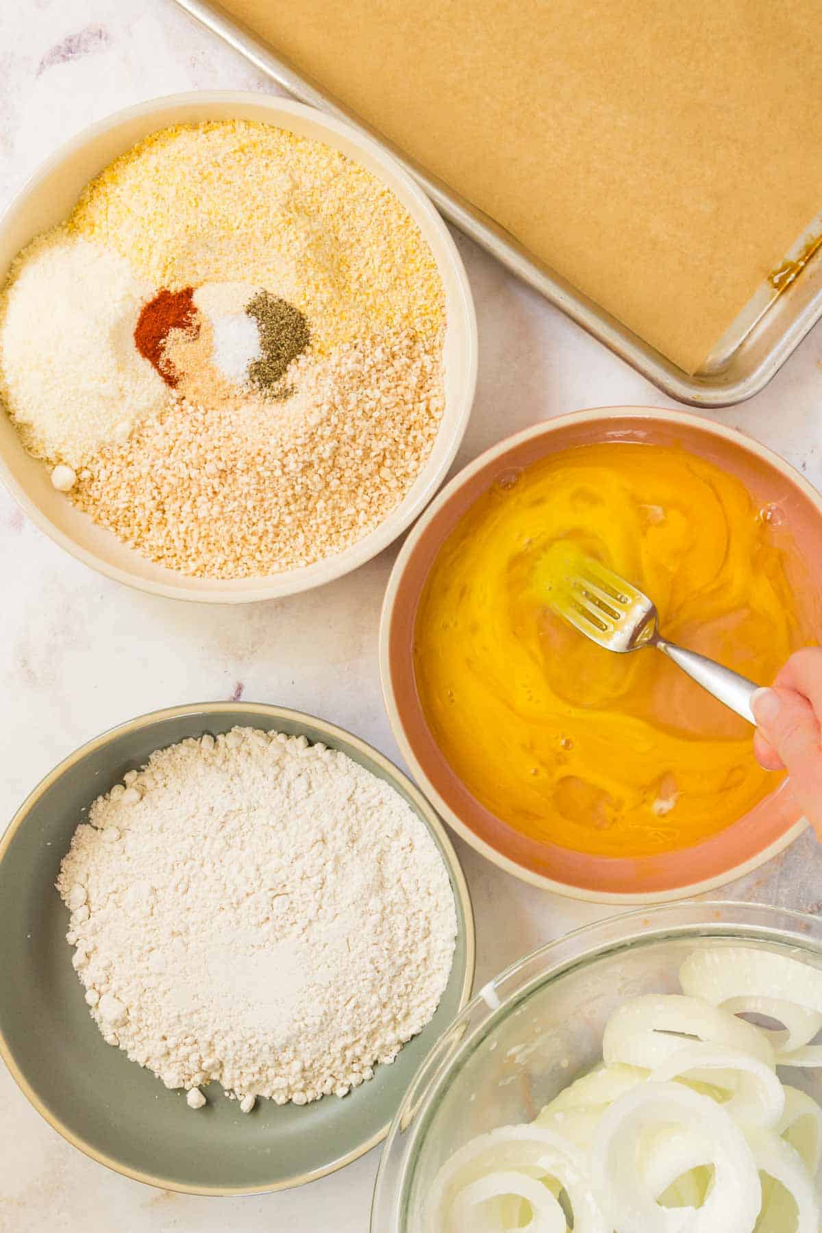 The various coating and breading ingredients in separate bowls, next to a baking tray.