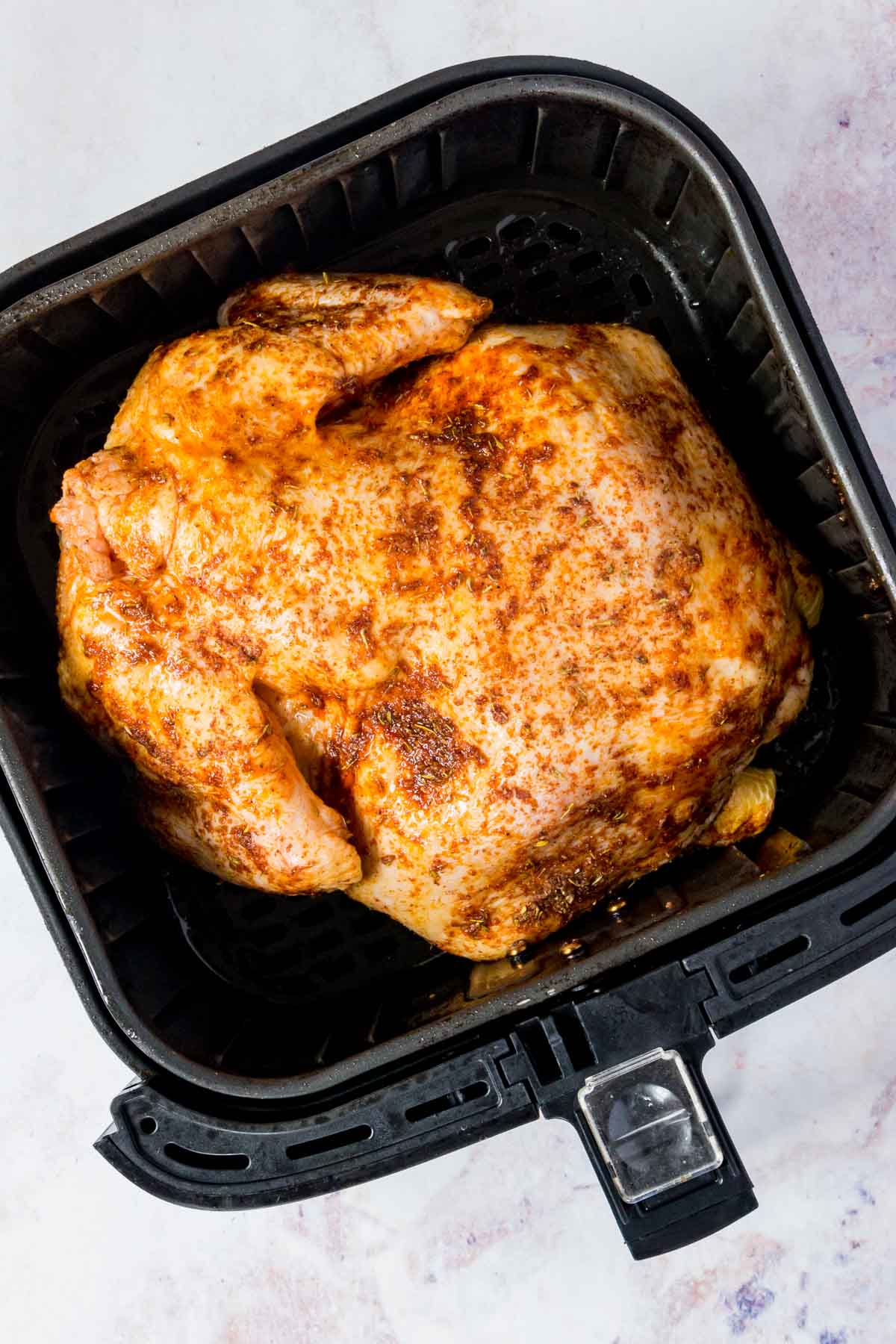 A whole seasoned chicken cooks inside the basket of an air fryer.