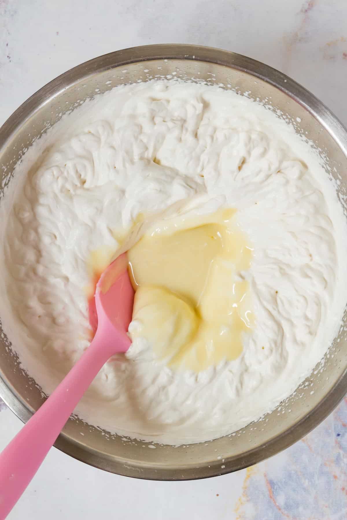 Condensed milk is stirred into whipping cream in a mixing bowl.