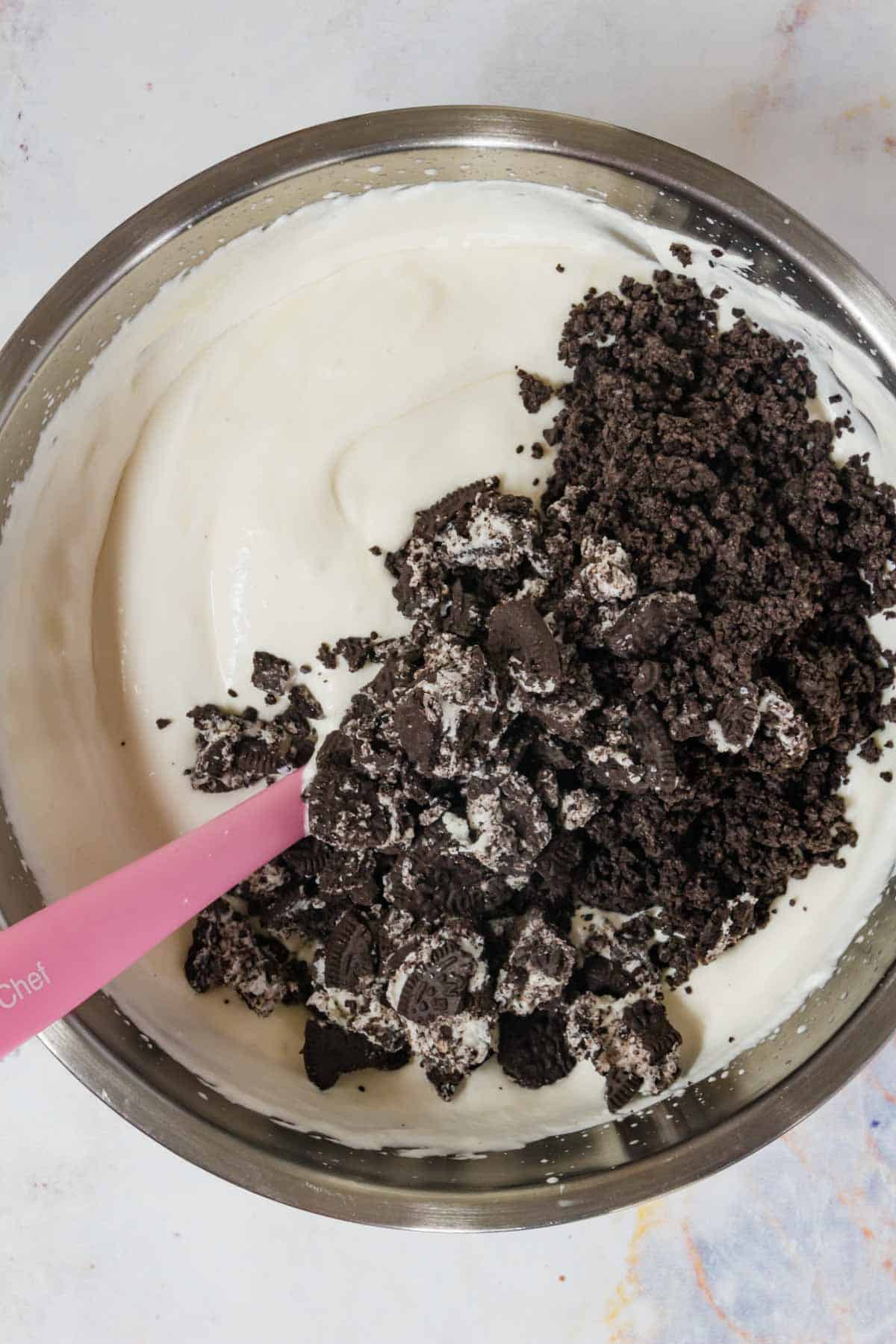 Crushed chocolate sandwich cookies are added into a mixing bowl with the vanilla ice cream base.
