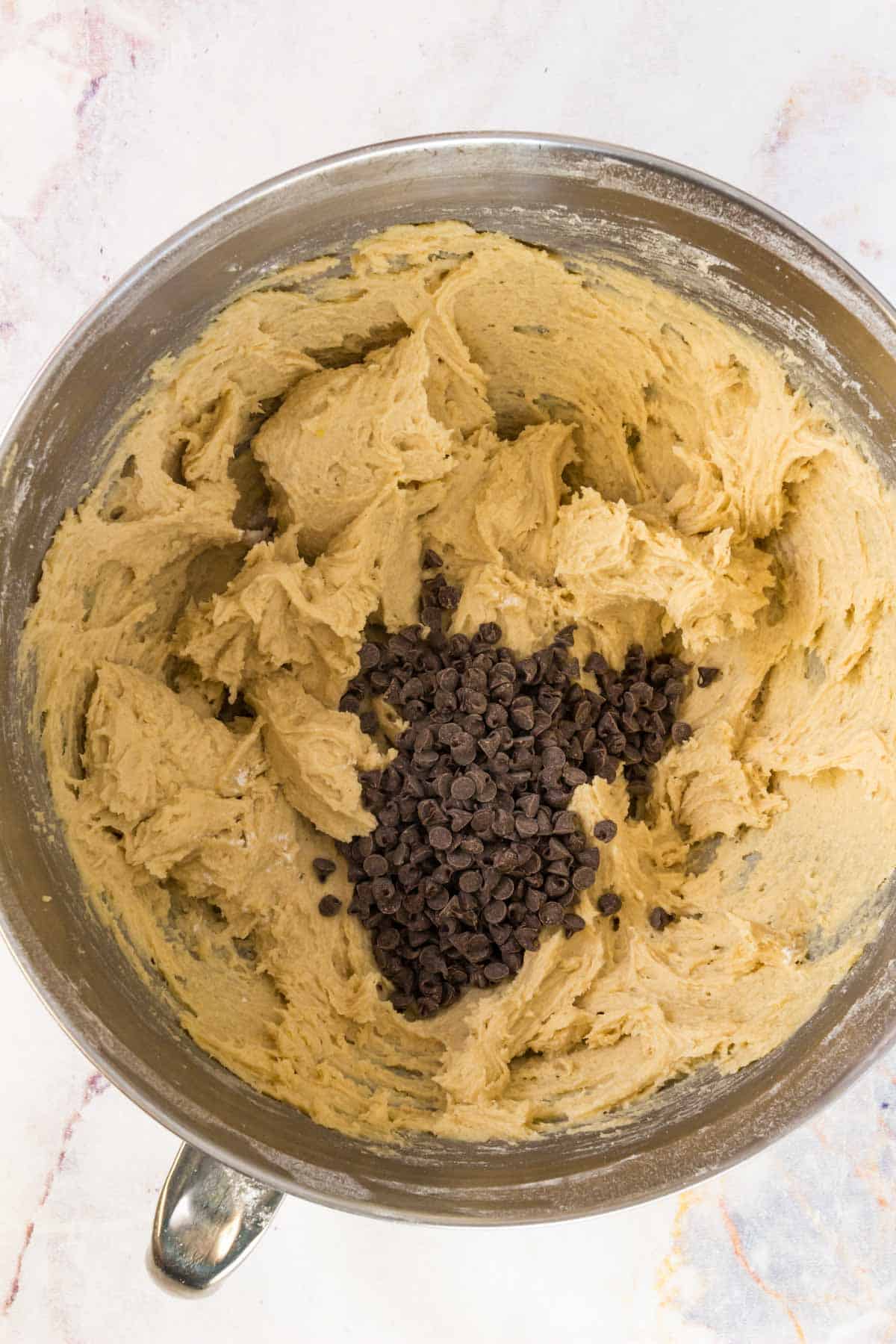 Mini chocolate chips are added into a mixing bowl with gluten free cookie dough.