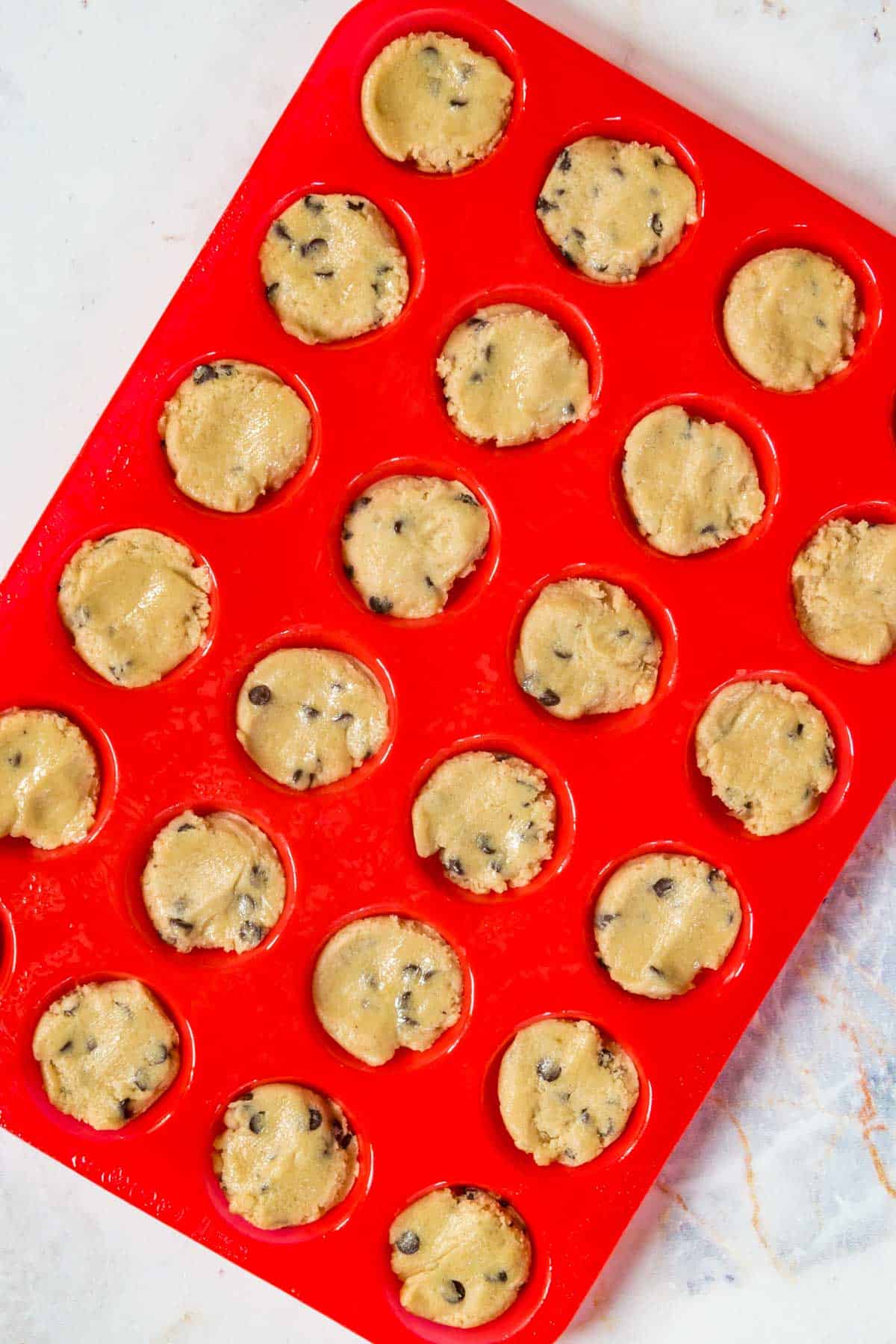 A silicone mini muffin tray filled with chocolate chip cookie dough.
