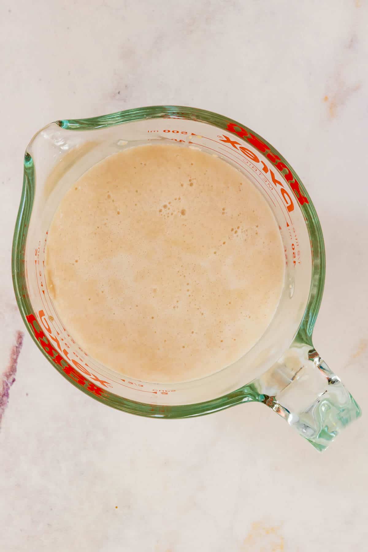 Yeast is dissolved in warm water in a glass measuring cup.