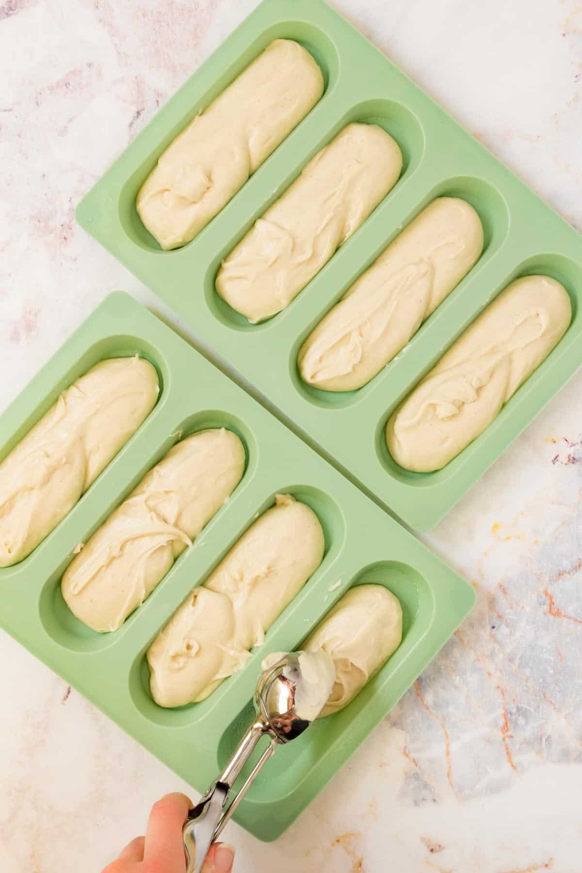 Gluten free hot dog bun dough is scooped into green silicone hot dog bun molds.