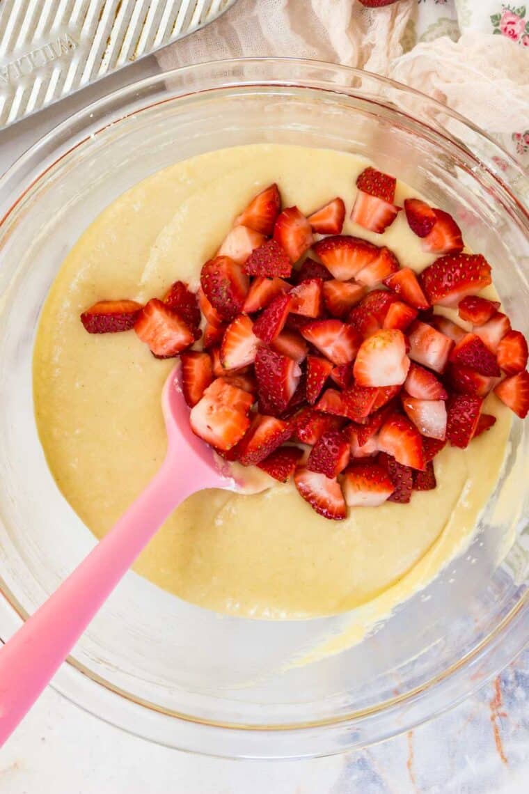 Chopped strawberries added into the strawberry muffin batter, stirred by a pink spoon.