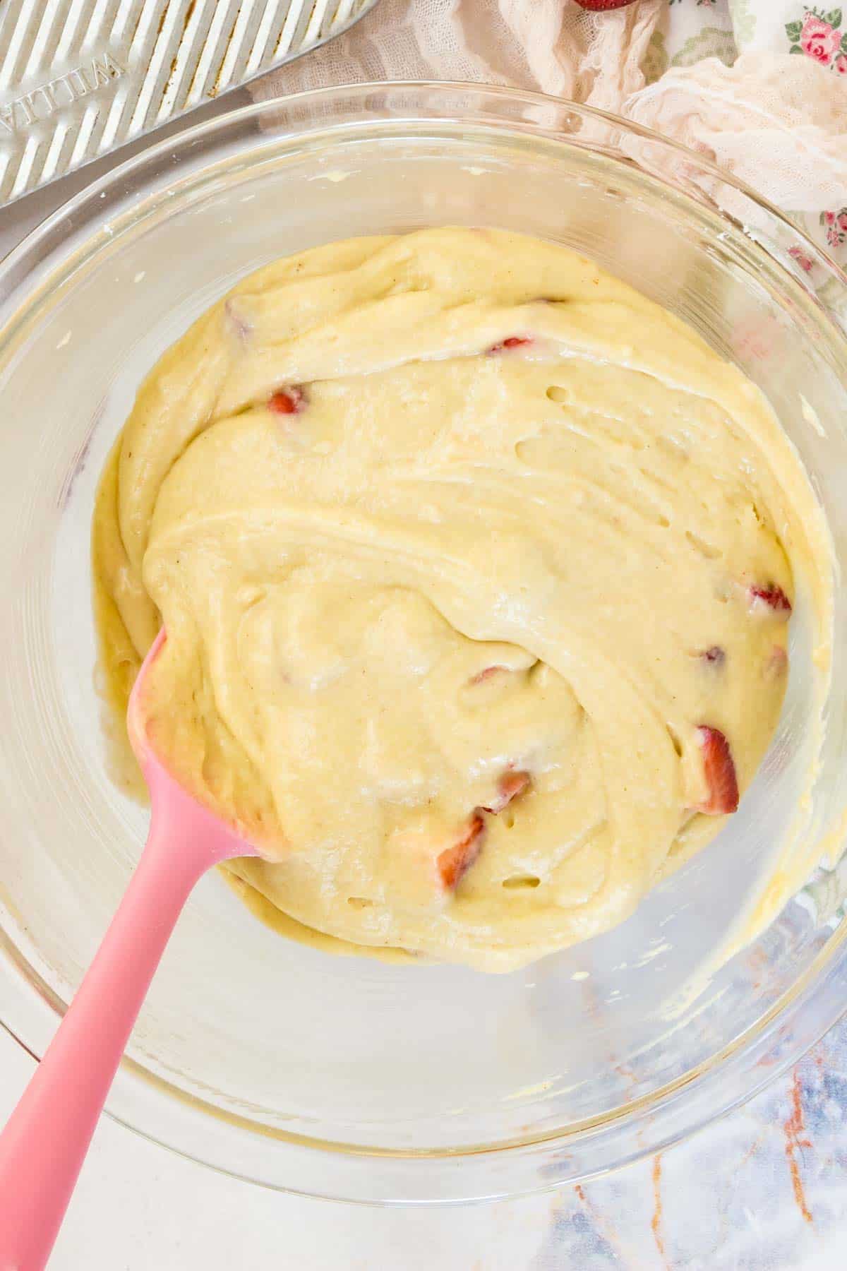 Strawberries are stirred into the muffin batter with a pink spoon.