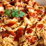 A bowl of pulled chicken drizzled with barbecue sauce.