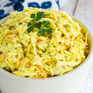 A bowl of mustard coleslaw with a sprig of parsley on top.