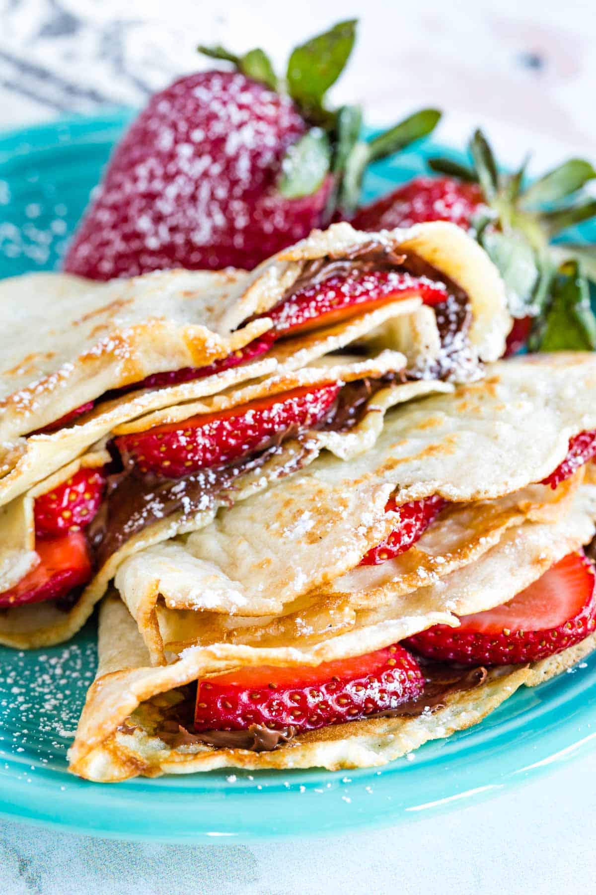 Two strawberry Nutella crepes with fresh strawberries on a blue plate.