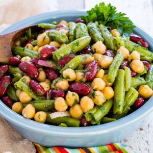 A blue bowl of three beans salad garnished with parsley.