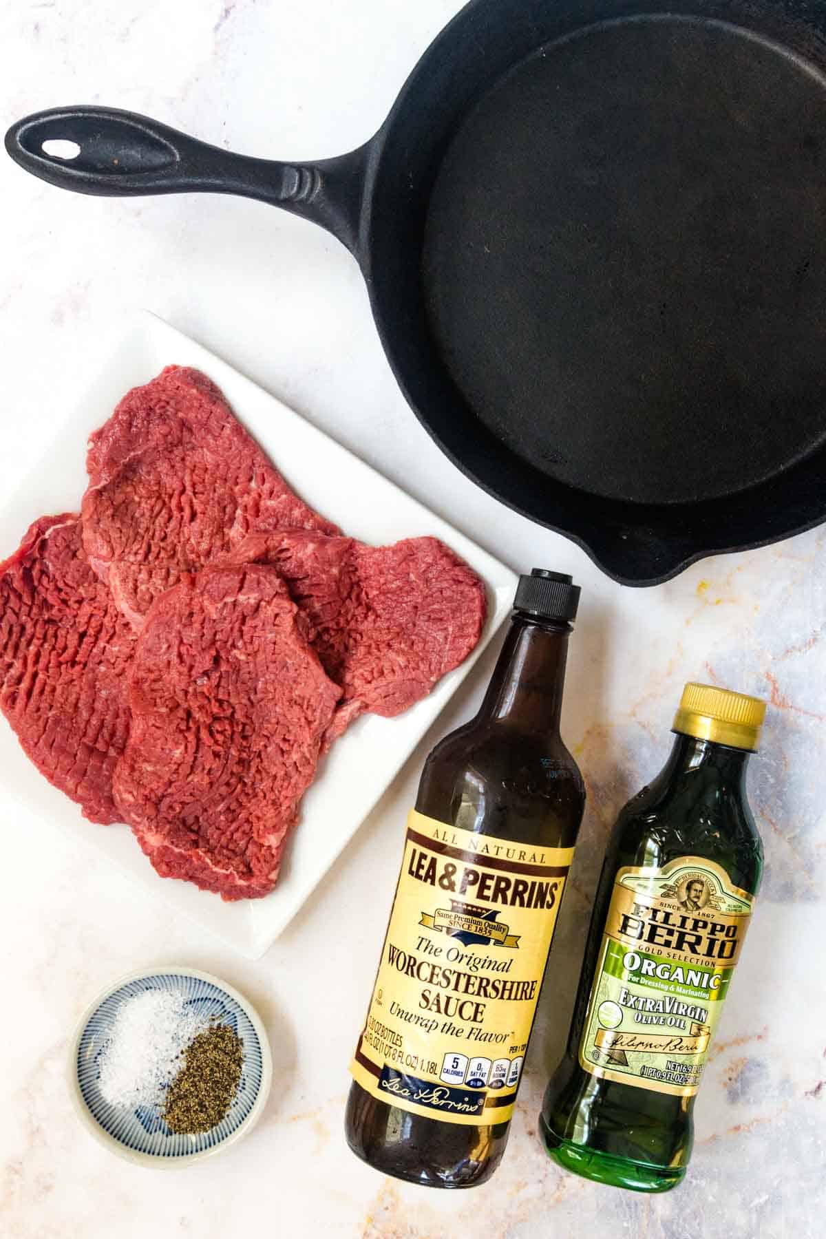 A cast iron skillet, uncooked cubed steaks, and other ingredients to make pan-seared cube steaks.