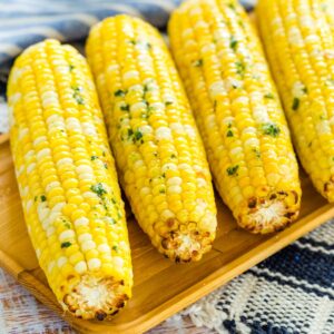 Air fryer corn on the cob coated with herb butter, lined up on a wooden serving platter.