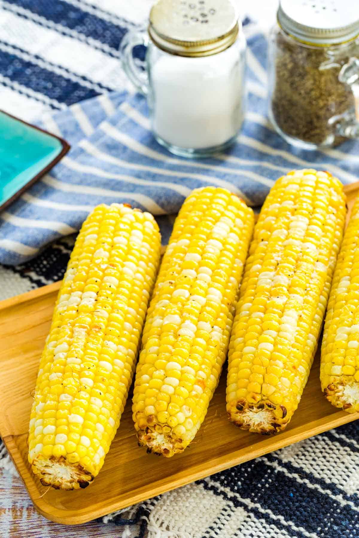 Air fryer corn on the cob lined up on a rectangular wooden serving platter, next to salt and pepper shakers.