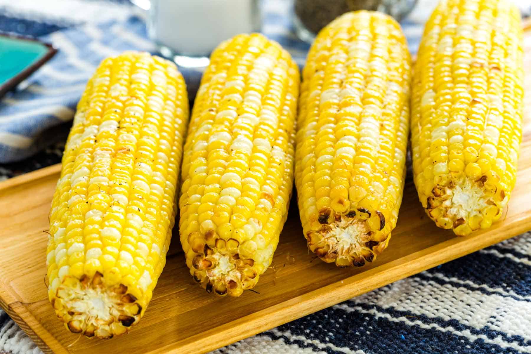 Air fryer corn on the cob lined up on a rectangular wooden serving platter, next to salt and pepper shakers.