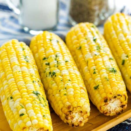 Air fryer corn on the cob lined up on a rectangular wooden serving platter, next to salt and pepper shakers.