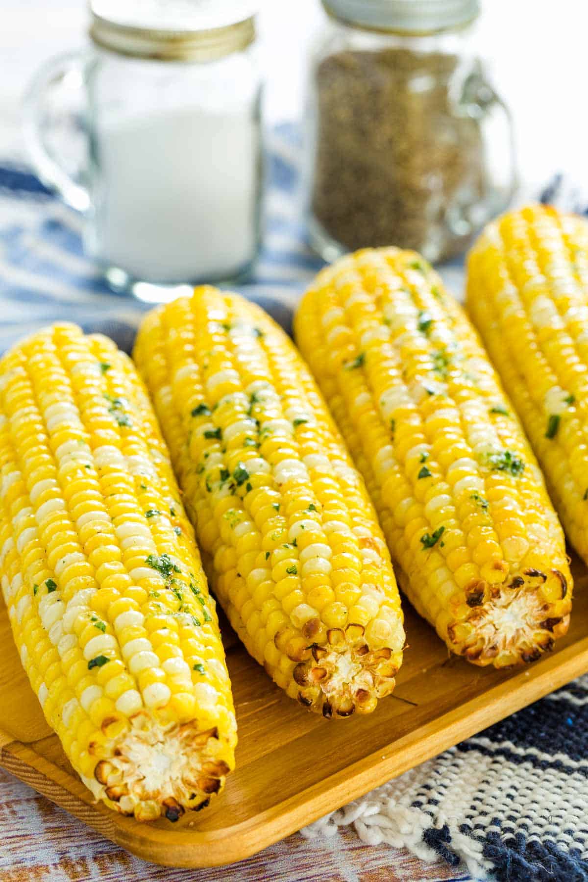 Air fryer corn on the cob lined up on a rectangular wooden serving platter, next to salt and pepper shakers.