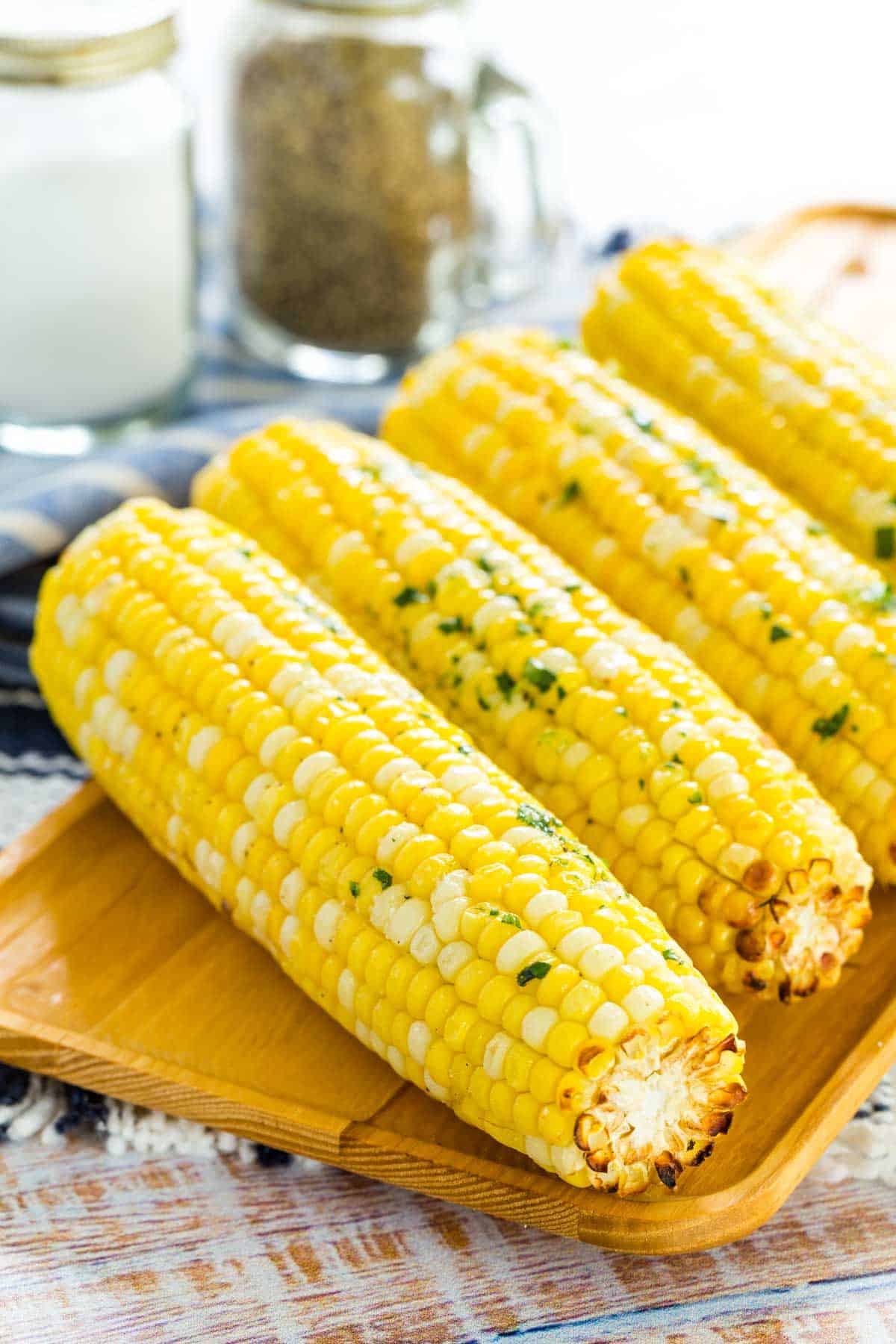 Close up of air fryer corn on the cob lined up on a rectangular wooden serving platter.