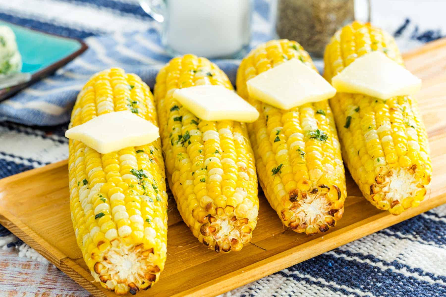 Air fryer corn on the cob topped with butter, lined up on a rectangular wooden serving platter.