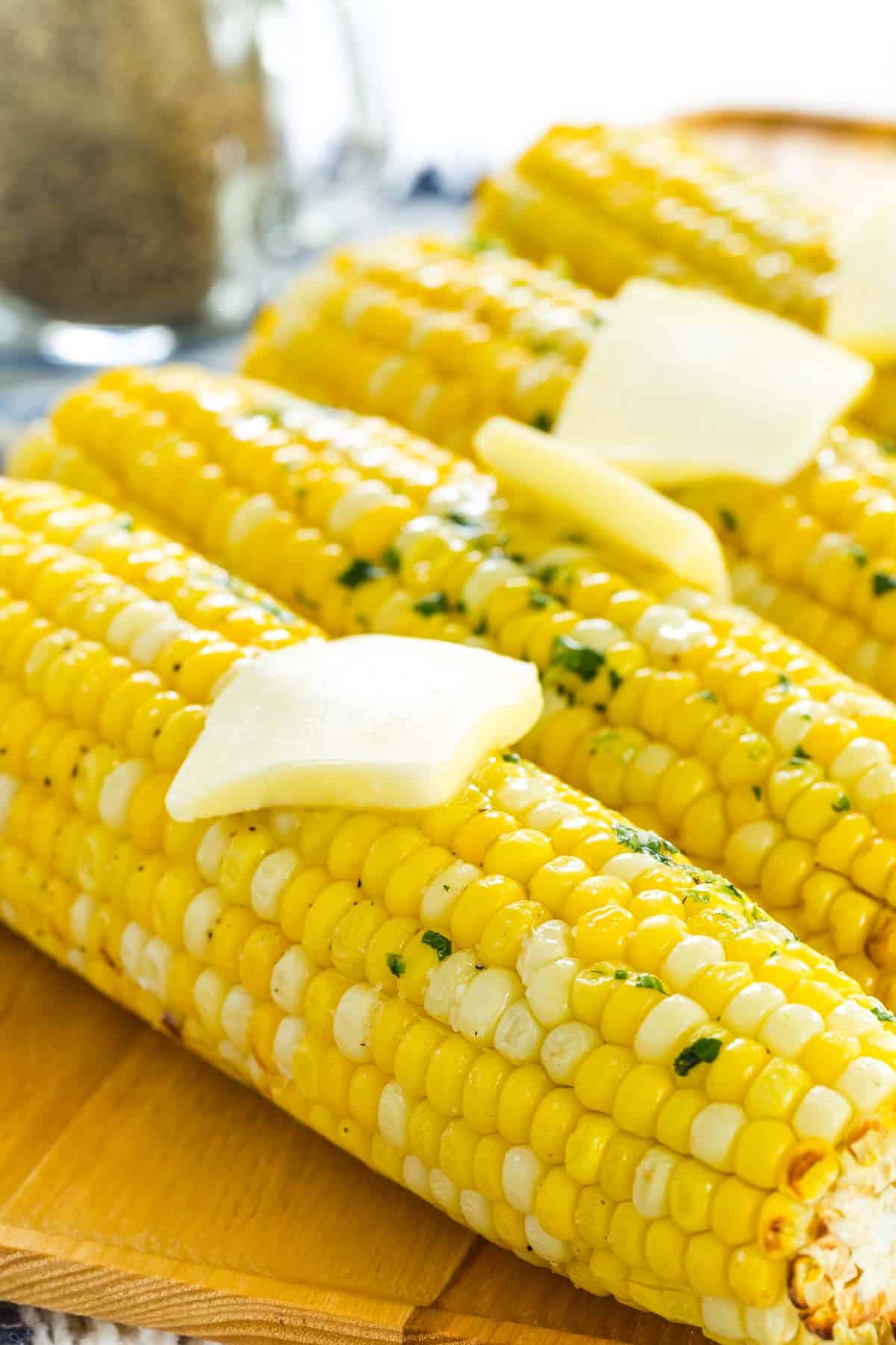 Close up of air fryer corn on the cob topped with butter, lined up on a rectangular wooden serving platter.