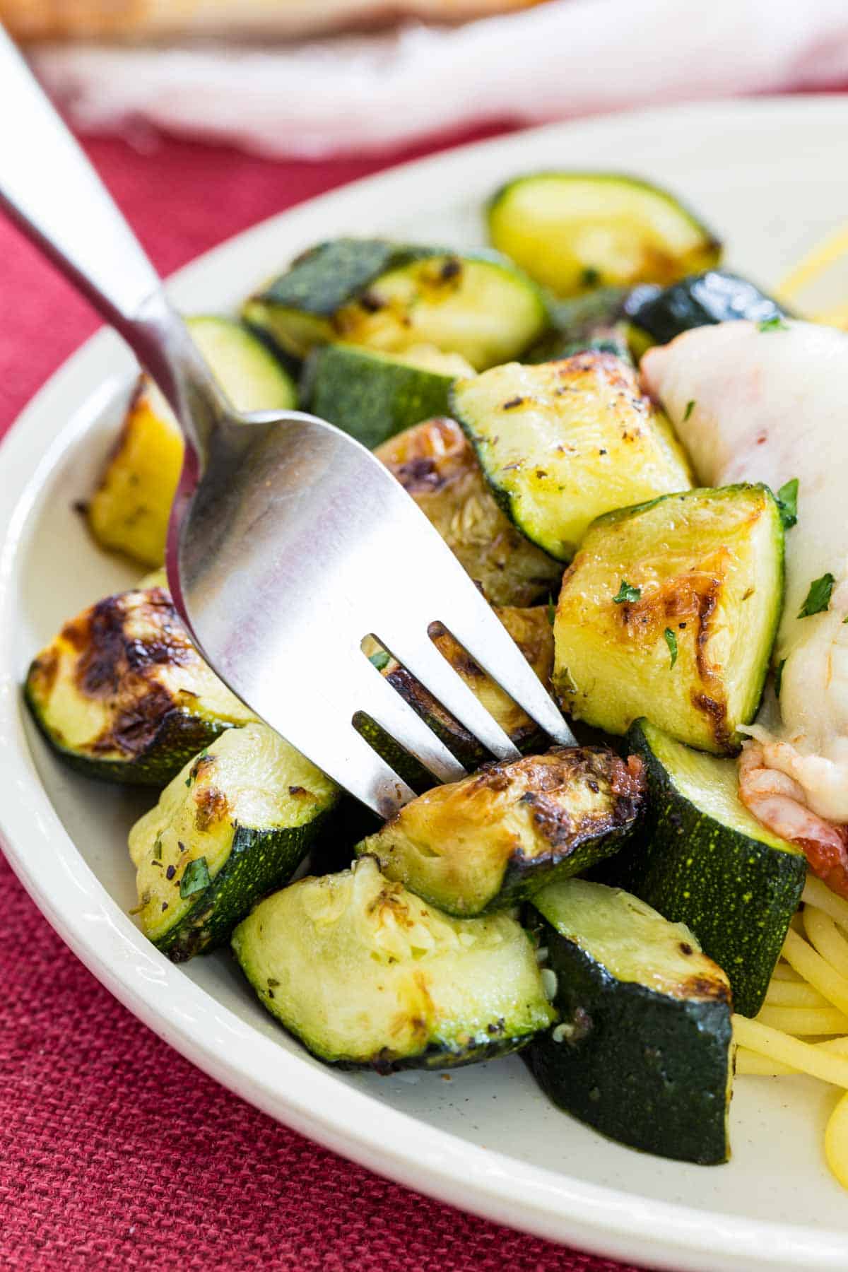 A fork picks up a piece of air fried zucchini from a white dish.