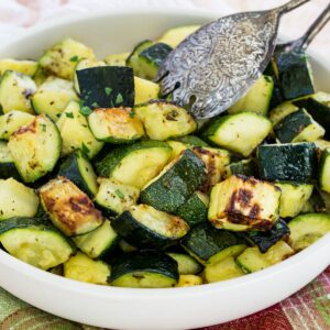 A bowl of roasted air fryer zucchini with silver serving tongs.