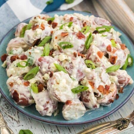 A bowl of potato slaad with bacon and blue cheese that is garnished with sliced scallions.