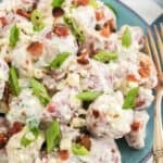 A blue bowl of potato salad with bacon and blue cheese for a fork set in it.