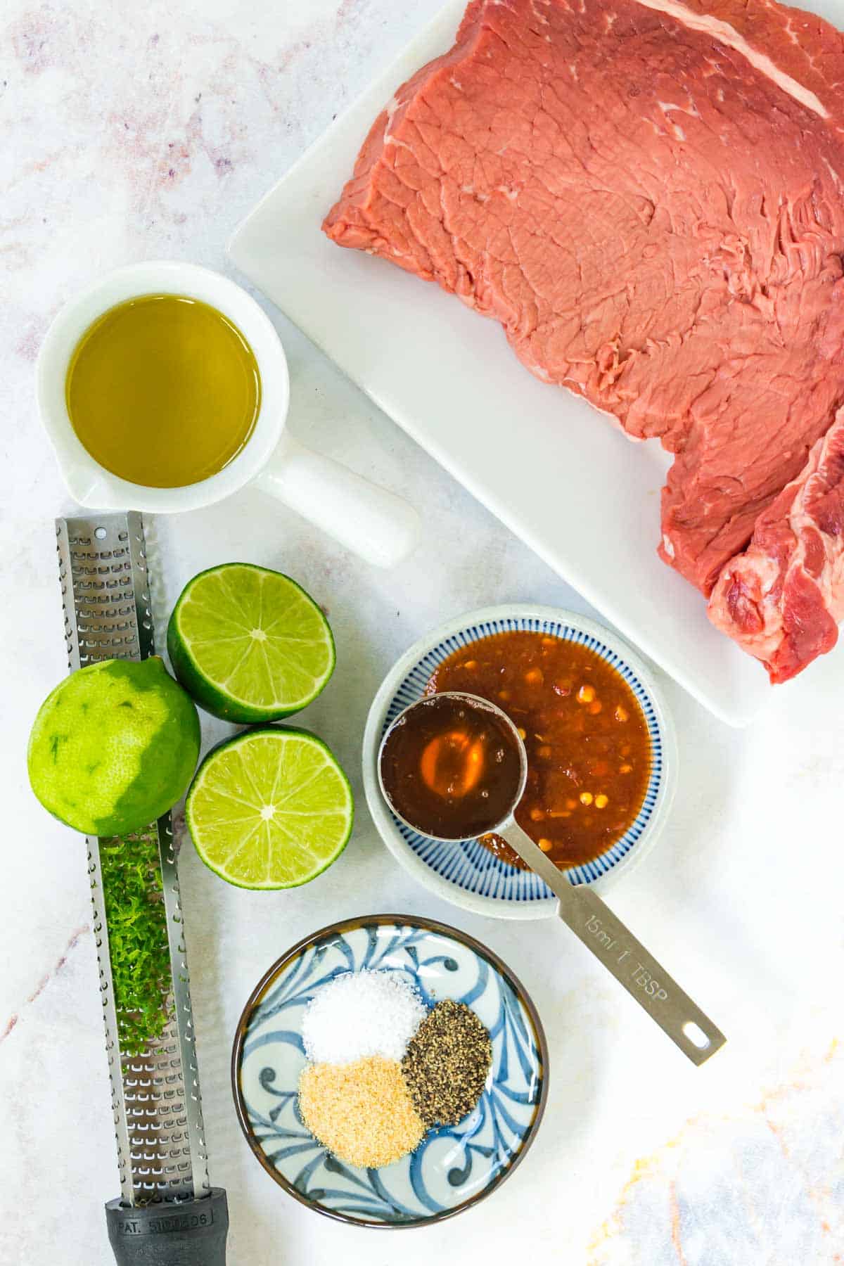 Ingredients to make chili lime steak bites in bowls with a handheld zester on a marble table