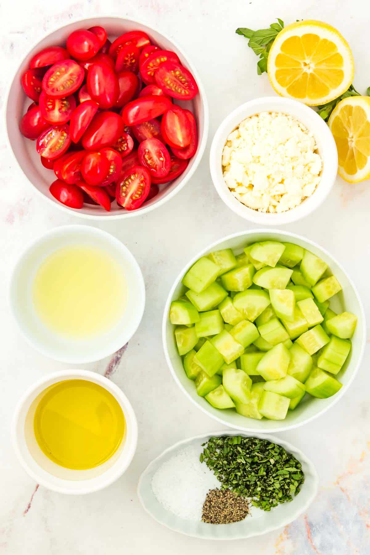 Bowls of sliced grape tomatoes, chopped cucumber, and other ingredients to make the salad.