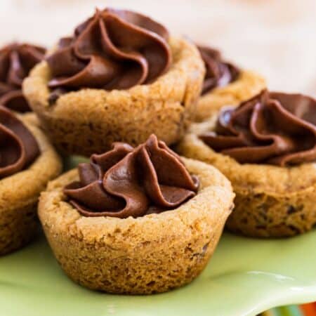 Chocolate chip cookie cups filled with chocolate frosting stacked on a green platter.