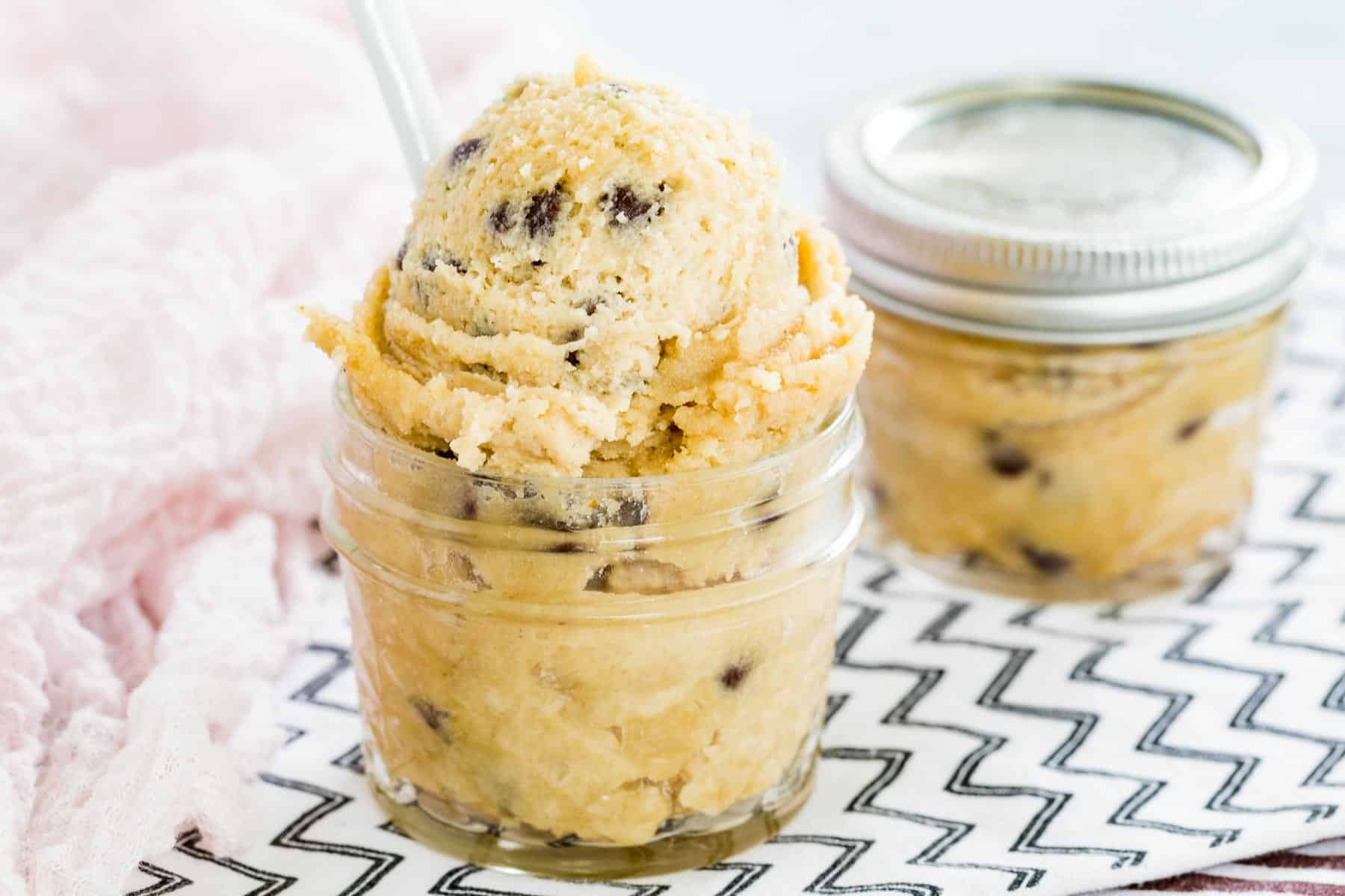 Gluten-free chocolate chip cookie dough in a glass jar with a white spoon.