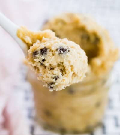 Close up of a spoonful of chocolate chip cookie dough, with a jar of dough in the background.