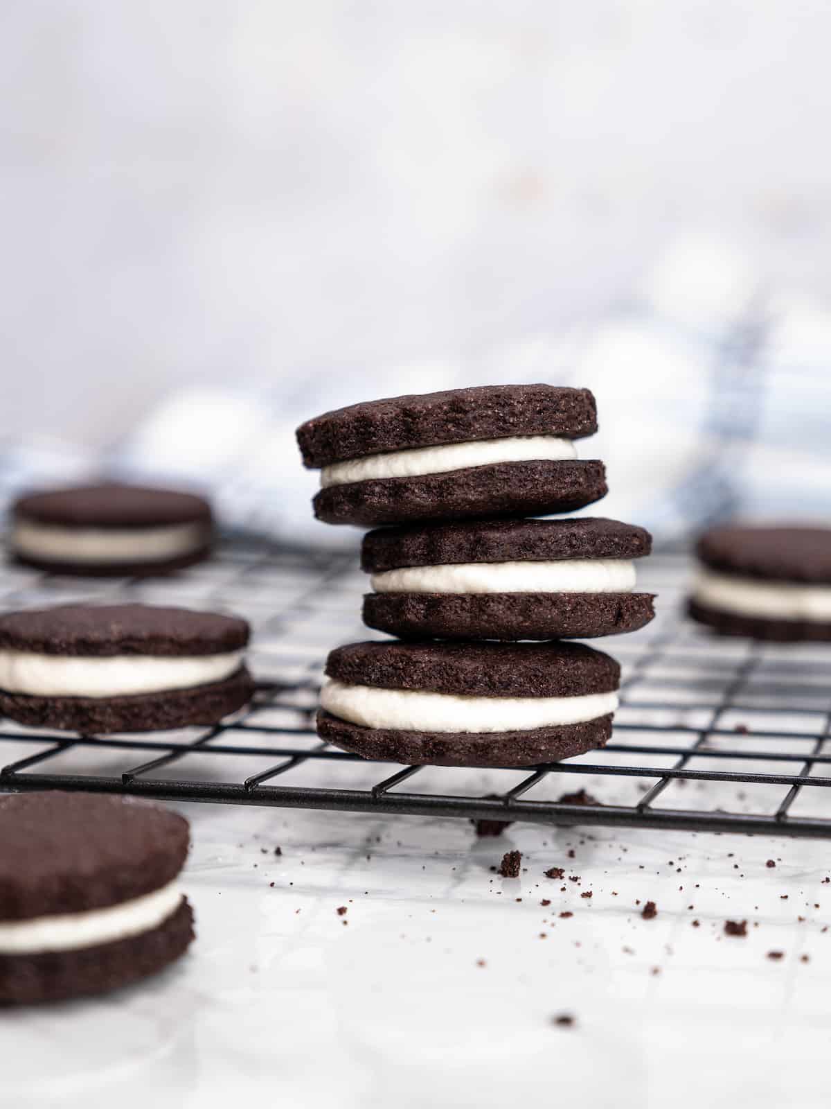 Three gluten free Oreos stacked on a wire rack next to more scattered Oreo cookies.